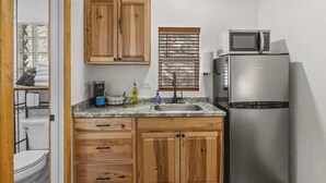 A compact kitchen with wooden cabinets, a stainless steel refrigerator, a microwave, and a window with blinds. - Cabin 18 - King Bed, Mountain views! Hotel Style! (Estes Park)