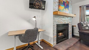 Een moderne woonkamer met een open haard, een wandgemonteerde televisie en een bureau met een stoel.