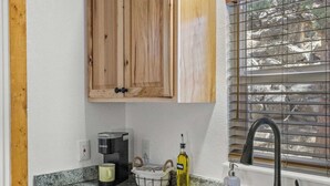 Een keuken met houten kastjes, een granieten aanrecht, een ingebouwde gootsteen, een koffiezetapparaat en een raam met zonwering.