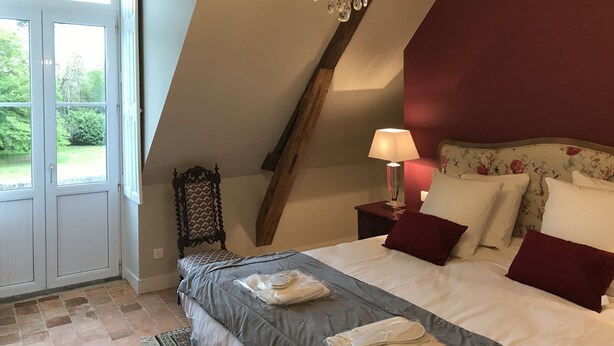 Een slaapkamer met een schuine plafond, een kroonluchter, een bed met kussens, een nachtkastje en een stoel.