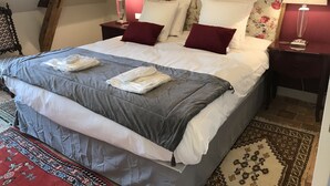 Een net opgemaakt bed met een grijze deken, witte lakens, twee bedlampjes en een hoofdbord met bloemen.