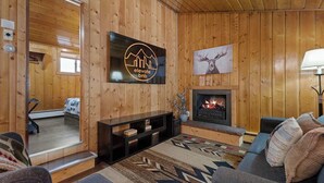 Ein Zimmer mit Holzwänden, einem Kamin, einer Couch, einem an der Wand befestigten Fernseher und einem Deckenventilator.