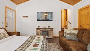 A cozy room with a bed, a brown sofa, a fireplace, and a wooden ceiling.