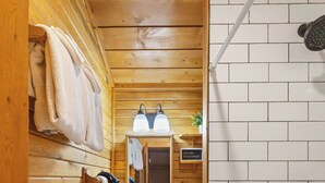 Un interior de madera con pared de azulejos blancos, un banco de madera con toallas, un lavabo y una bañera.