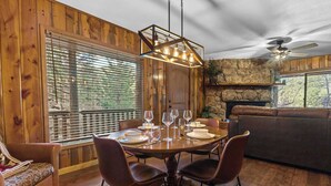 A wooden-paneled room with a round dining table set for four, a sofa, and a fireplace.
