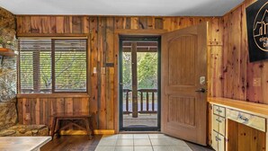 A wooden interior with a door leading to an outdoor deck, a small table, and a cabinet with drawers.