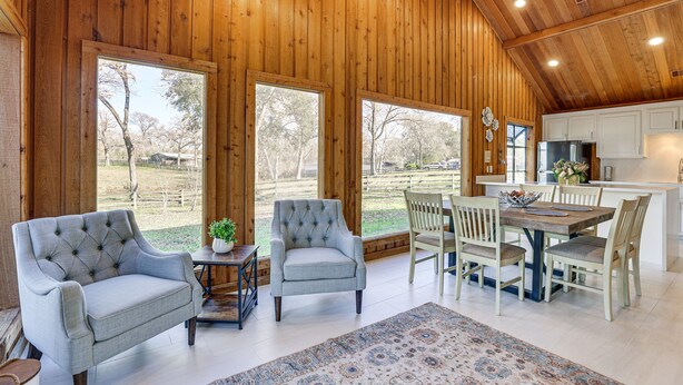 A spacious room with wooden walls, a dining area with a table and chairs, and large windows offering a view of the outdoors. - Hot Tub, Deck & Grill: Brookshire Gem Near Venues (Brookshire)