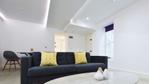 Un salon moderne avec un canapé gris foncé, deux coussins jaunes à motifs, une table basse ronde en marbre et un fauteuil noir.