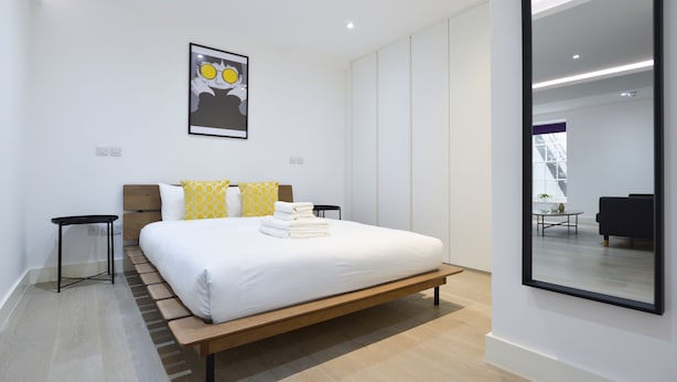 Une chambre moderne avec un grand lit, une table de chevet, un miroir et une œuvre d’art accrochée au mur.