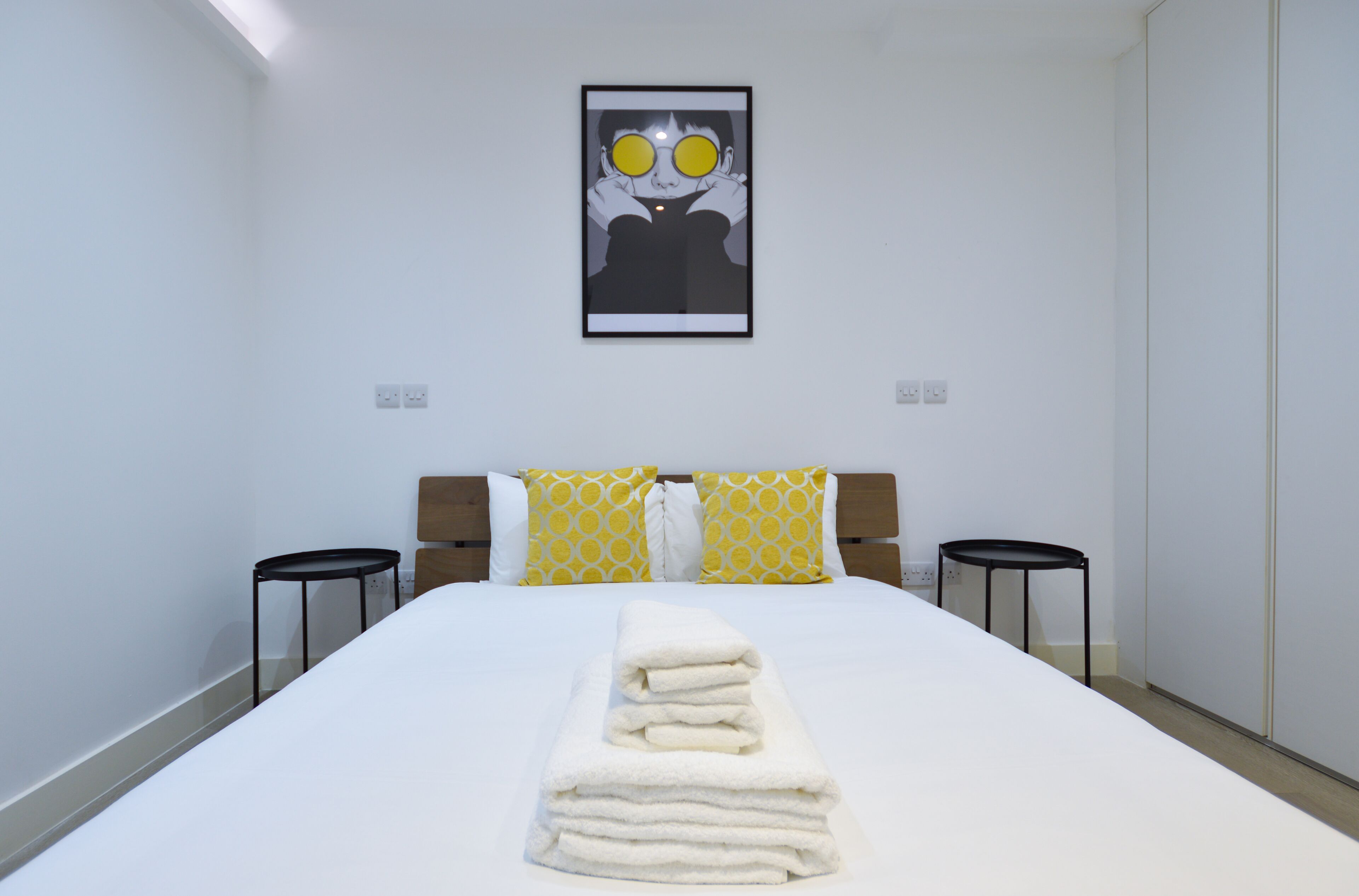 A hotel room with a neatly made bed, two bedside tables, and a framed artwork on the wall.
