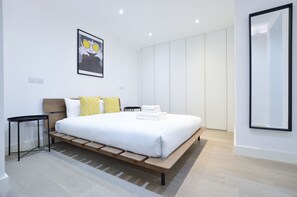 Un dormitorio moderno con una cama grande, una mesita de noche, un espejo en la pared y un cuadro enmarcado.