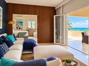 A modern living room with a sofa set, a coffee table with a plant, and a view of the ocean through a sliding glass door.