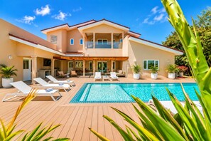 A two-story house with a swimming pool, outdoor seating, and potted plants.