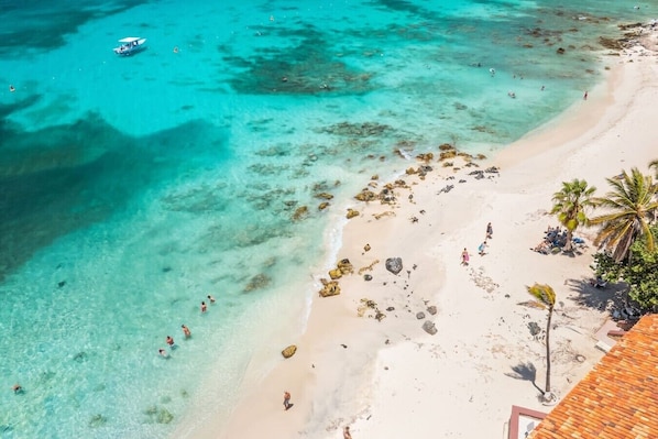 A beach with clear turquoise water, a boat, and people swimming.