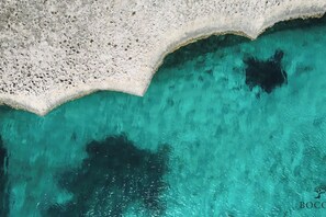 An aerial view of a coastal area with clear turquoise waters and a rocky shoreline.