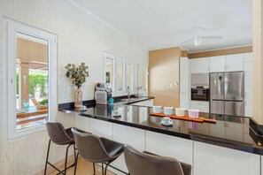 A modern kitchen with a central island, bar stools, stainless steel appliances, and a view of the outdoors.