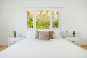 A bedroom with a large bed, two bedside tables, and a window with a view of greenery.