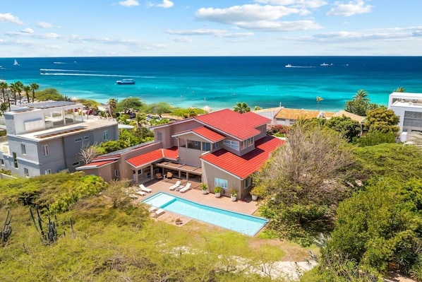 Une maison moderne à deux étages, avec un toit rouge, une piscine et une vue sur l’océan.