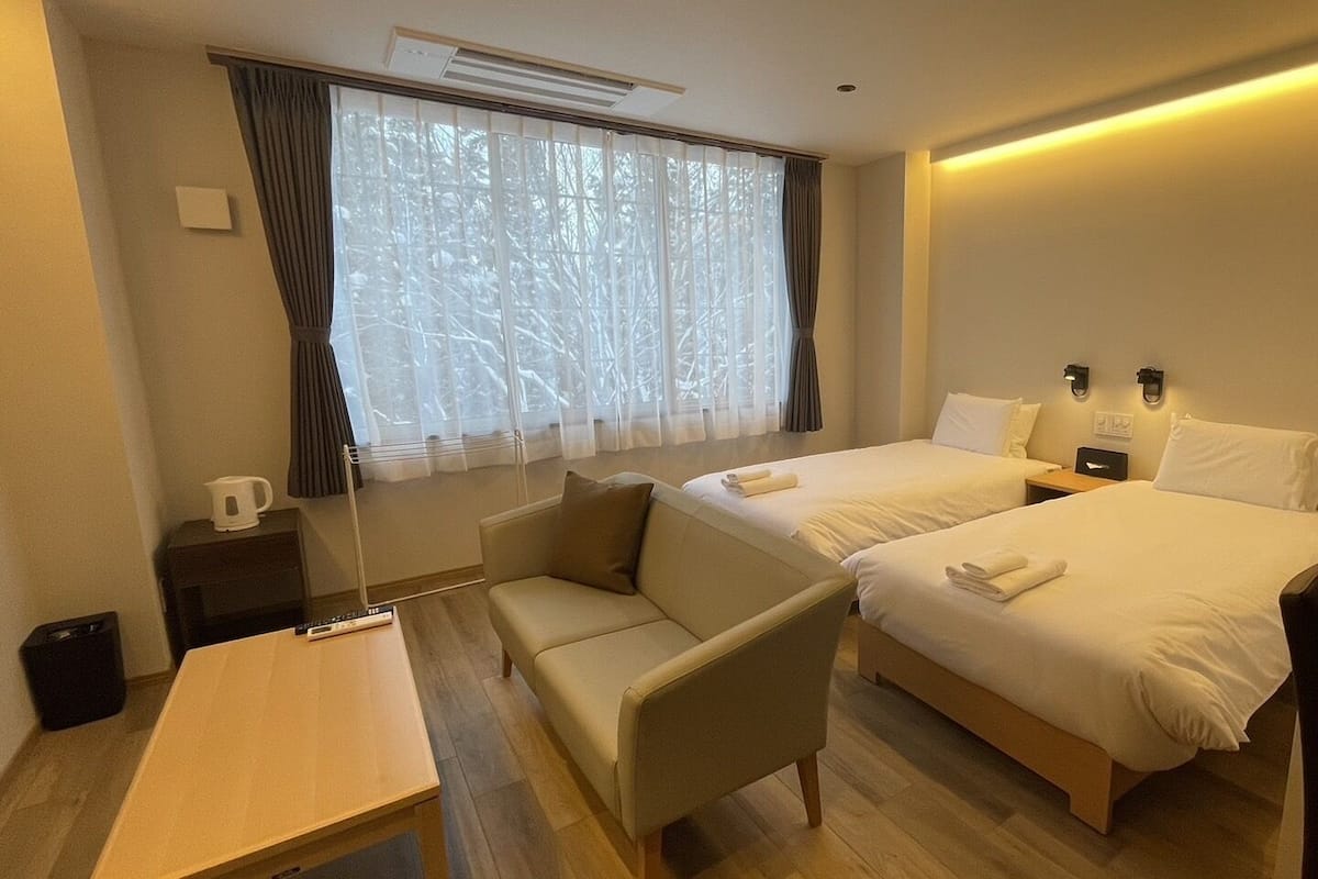 A hotel room with two beds, a sofa, a table, and a window with curtains.