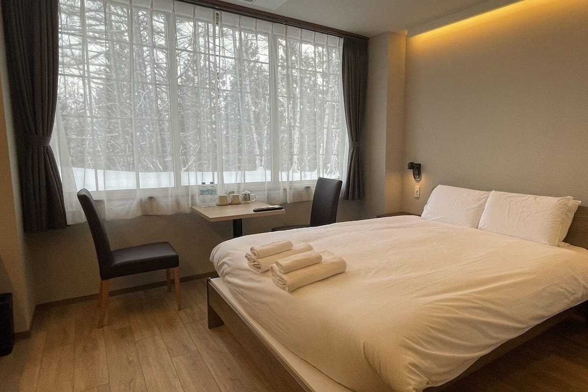 A hotel room with a large bed, a desk with a chair, and a window with curtains.