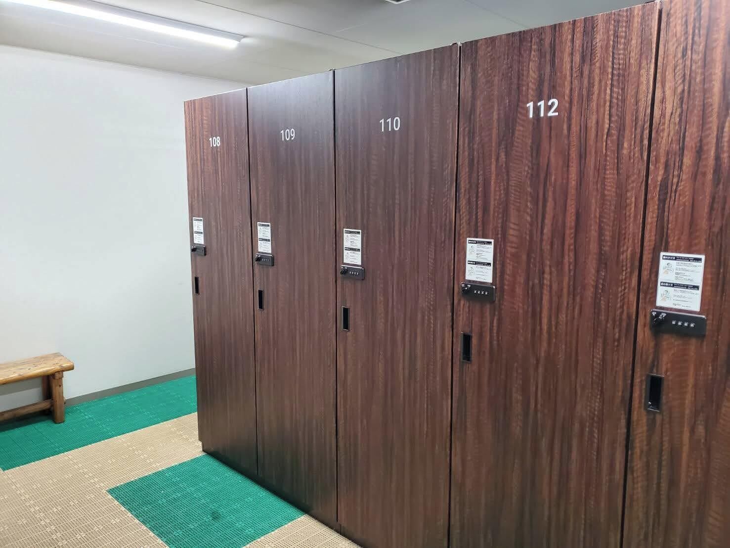 Una hilera de taquillas de madera numeradas del 108 al 112 en un pasillo con un felpudo verde y beige.
