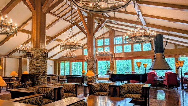 A spacious indoor area with high ceilings, wooden beams, and multiple chandeliers. There are several seating areas with tables and chairs, a piano, and a stone fireplace. - WHITE HOTEL GRAND HAKUBA (Omachi)