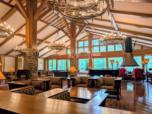 A spacious indoor area with high ceilings, wooden beams, and multiple chandeliers. There are several seating areas with tables and chairs, a piano, and a stone fireplace. - WHITE HOTEL GRAND HAKUBA (Omachi)