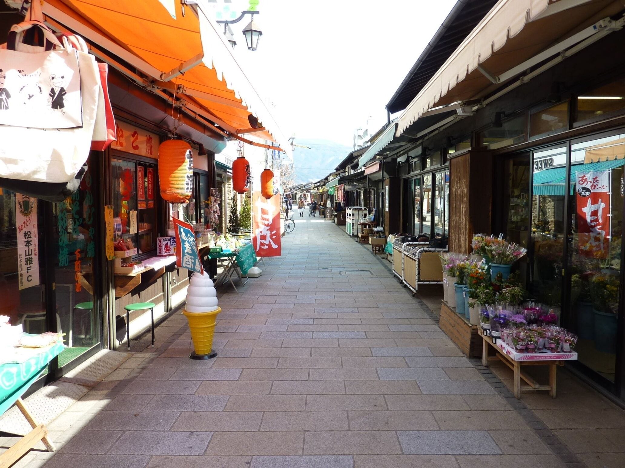 A narrow street with shops on both sides, a yellow cone-shaped object in the center, and traditional architecture.