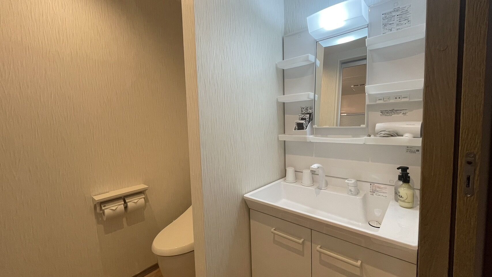 A bathroom with a toilet, a sink with a mirror, and a shelf above the sink.