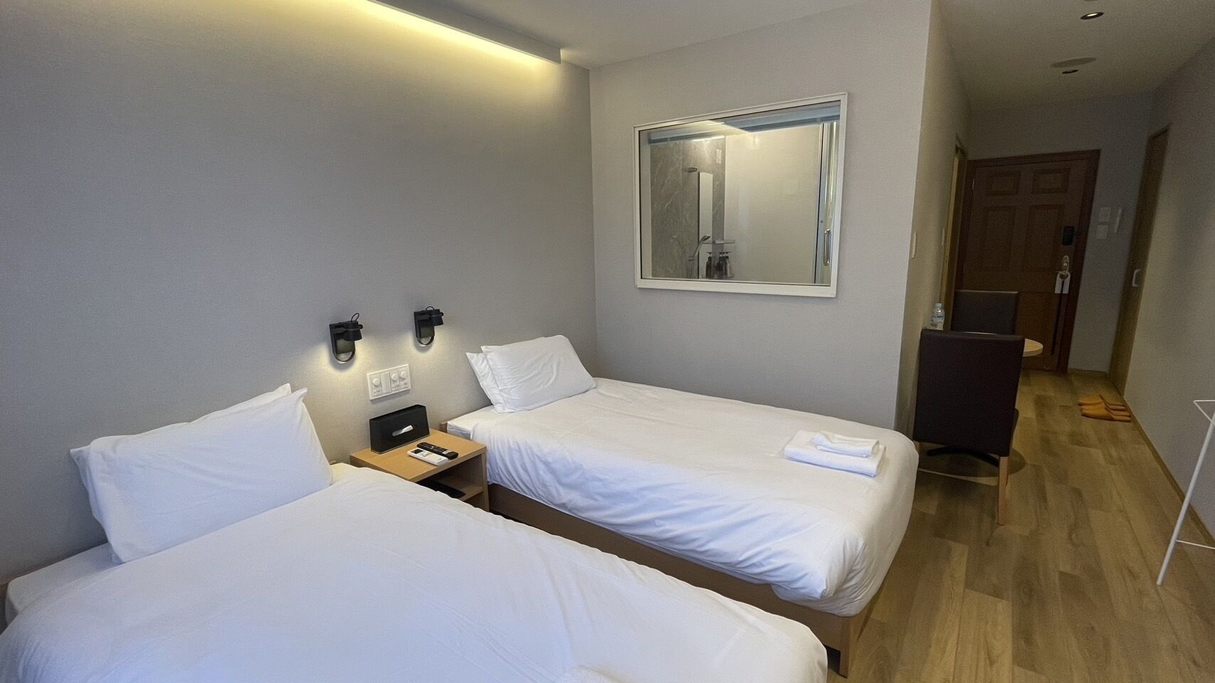 Une chambre d’hôtel avec deux lits, une table de chevet avec une lampe, un miroir au mur et un plancher en bois.
