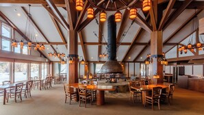A spacious dining area with wooden tables and chairs, a central fire pit, and a large wooden ceiling structure with hanging lanterns. - WHITE HOTEL GRAND HAKUBA (Omachi)
