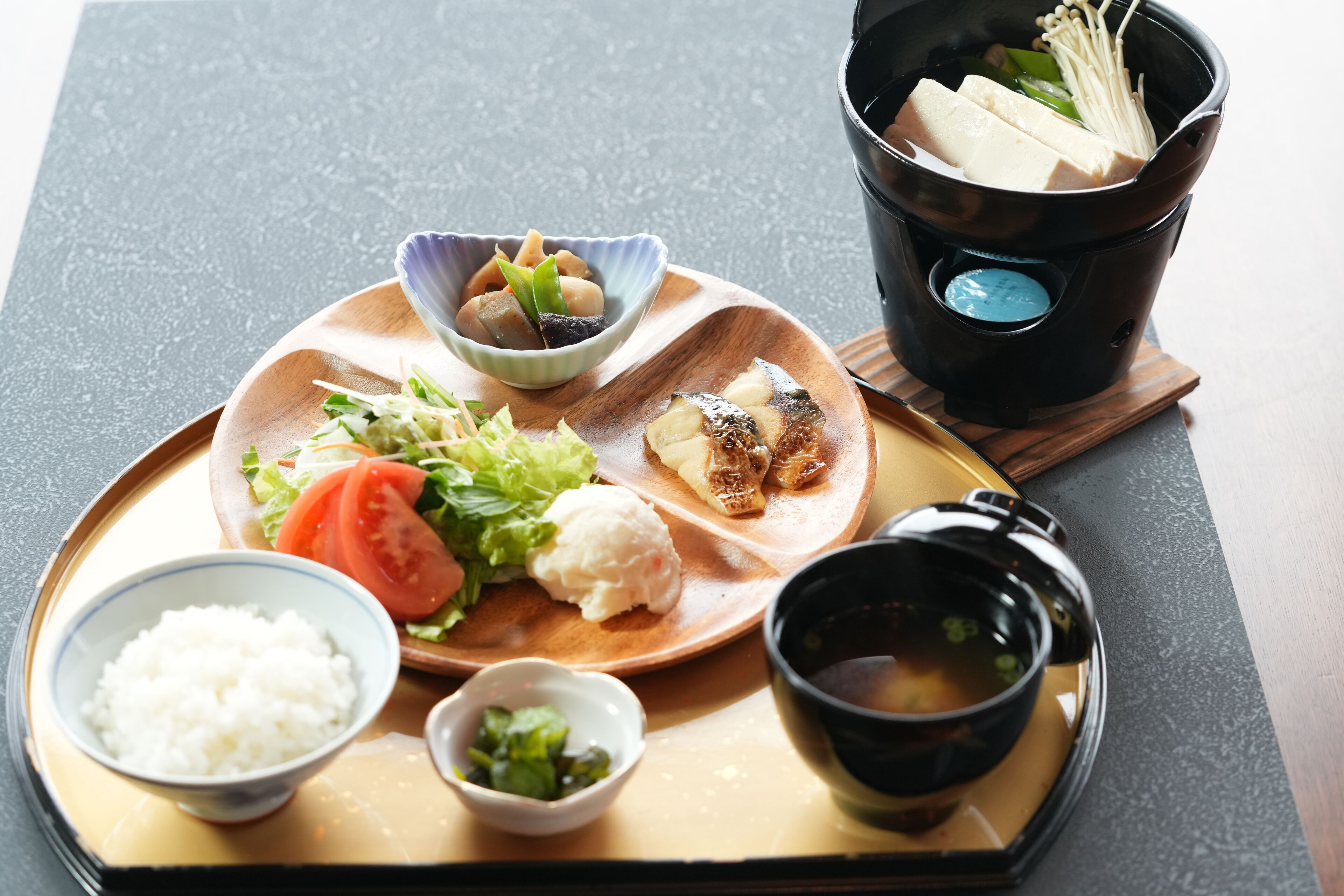 A traditional Japanese meal with rice, vegetables, fish, and tofu on a wooden tray.