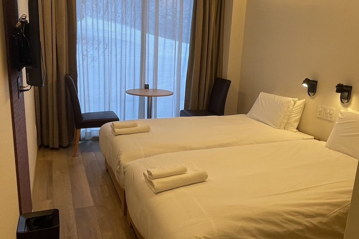 A hotel room with two beds, a small table, and a chair.