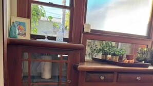 Un mueble de madera con puertas de cristal y cajones, una ventana con vistas a la vegetación, y una pequeña estantería con objetos decorativos.