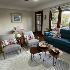 Un salon avec un canapé bleu, deux fauteuils, une table basse et une table d’appoint sur laquelle est posée une plante.