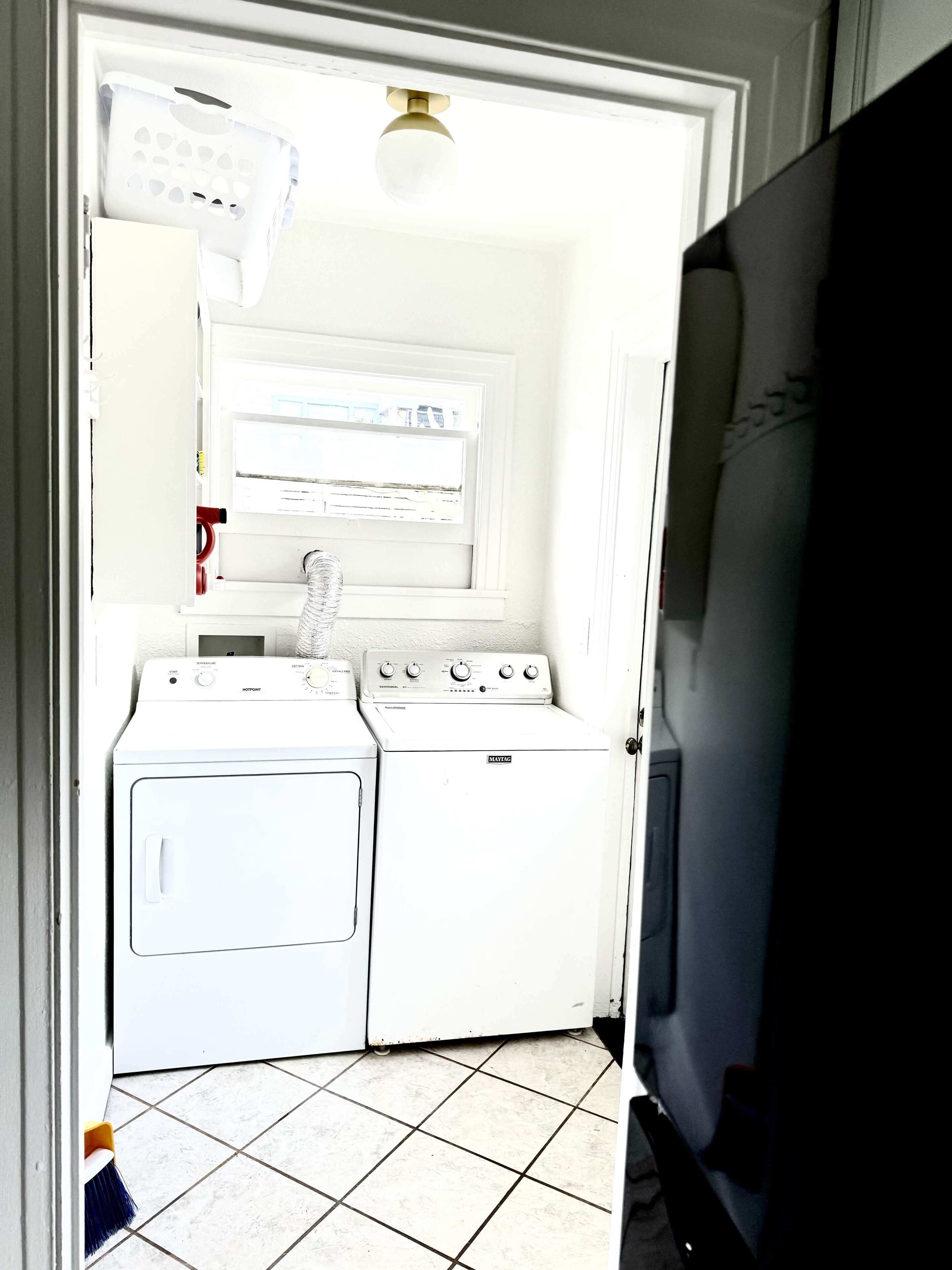 Un área de lavandería con lavadora y secadora, un termostato y una lámpara en el techo.
