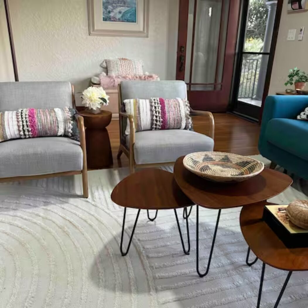 Una sala de estar acogedora con dos sofás grises, una mesita redonda de madera y un sillón azul.
