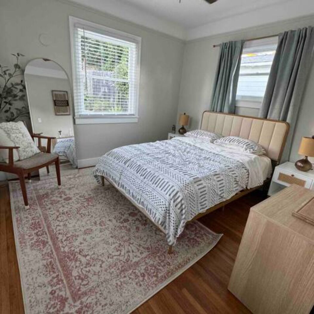 A bedroom with a bed, a nightstand, a chair, a window with blinds, and a rug.