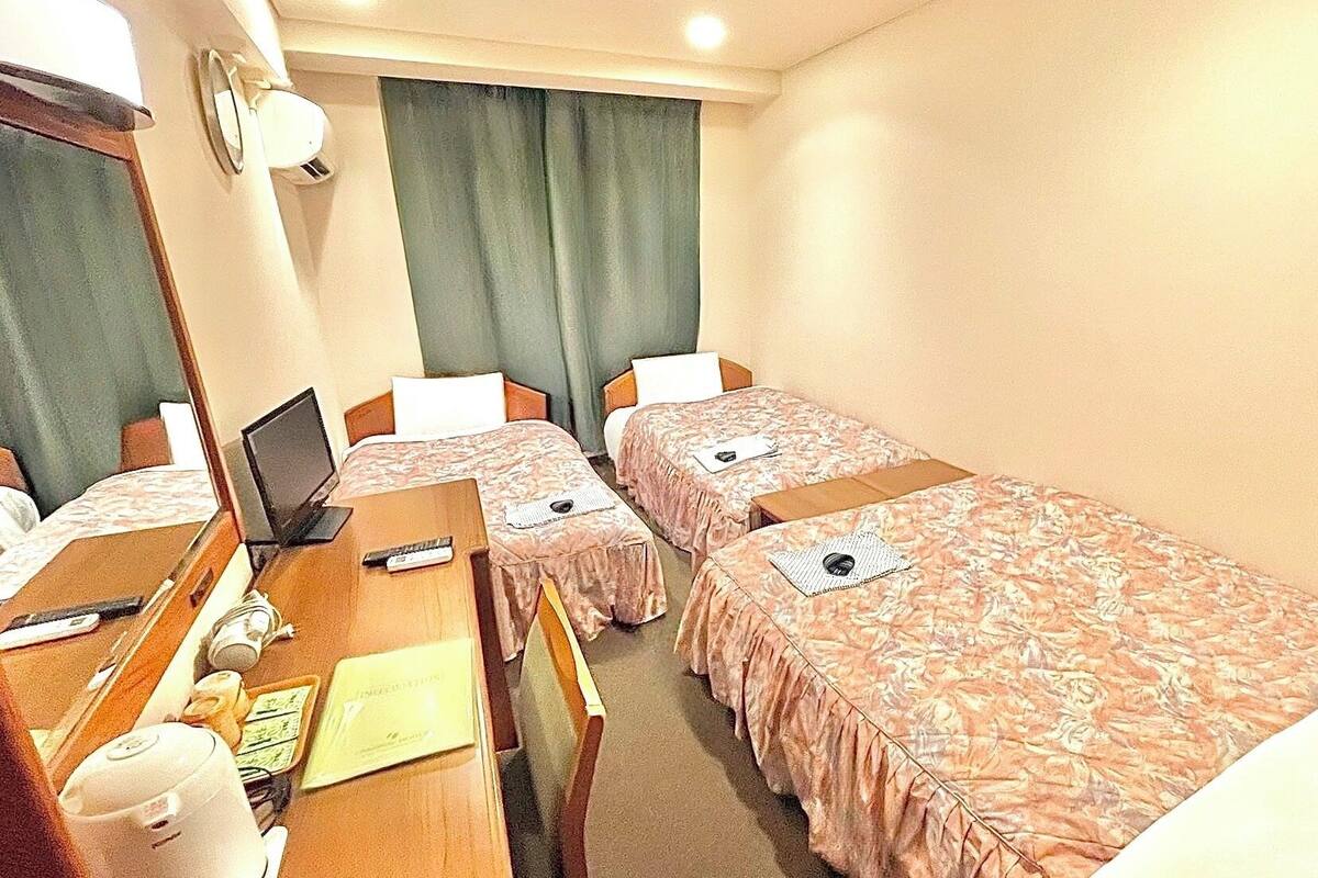 A hotel room with two single beds, a desk with a laptop, a chair, a small table with a cup, and a mirror.