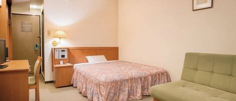 Une chambre d’hôtel avec un lit, un bureau, une chaise, une table de chevet avec une lampe et un canapé vert.