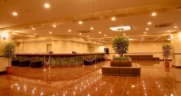 Welcome to our hotel lobby, featuring a polished tile floor, a reception desk with potted plants, and a comfortable seating area.