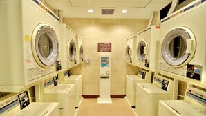 A laundromat with multiple washing machines and dryers, a central information kiosk, and a tiled floor. - Matsue Universalhotel   (Matsue)