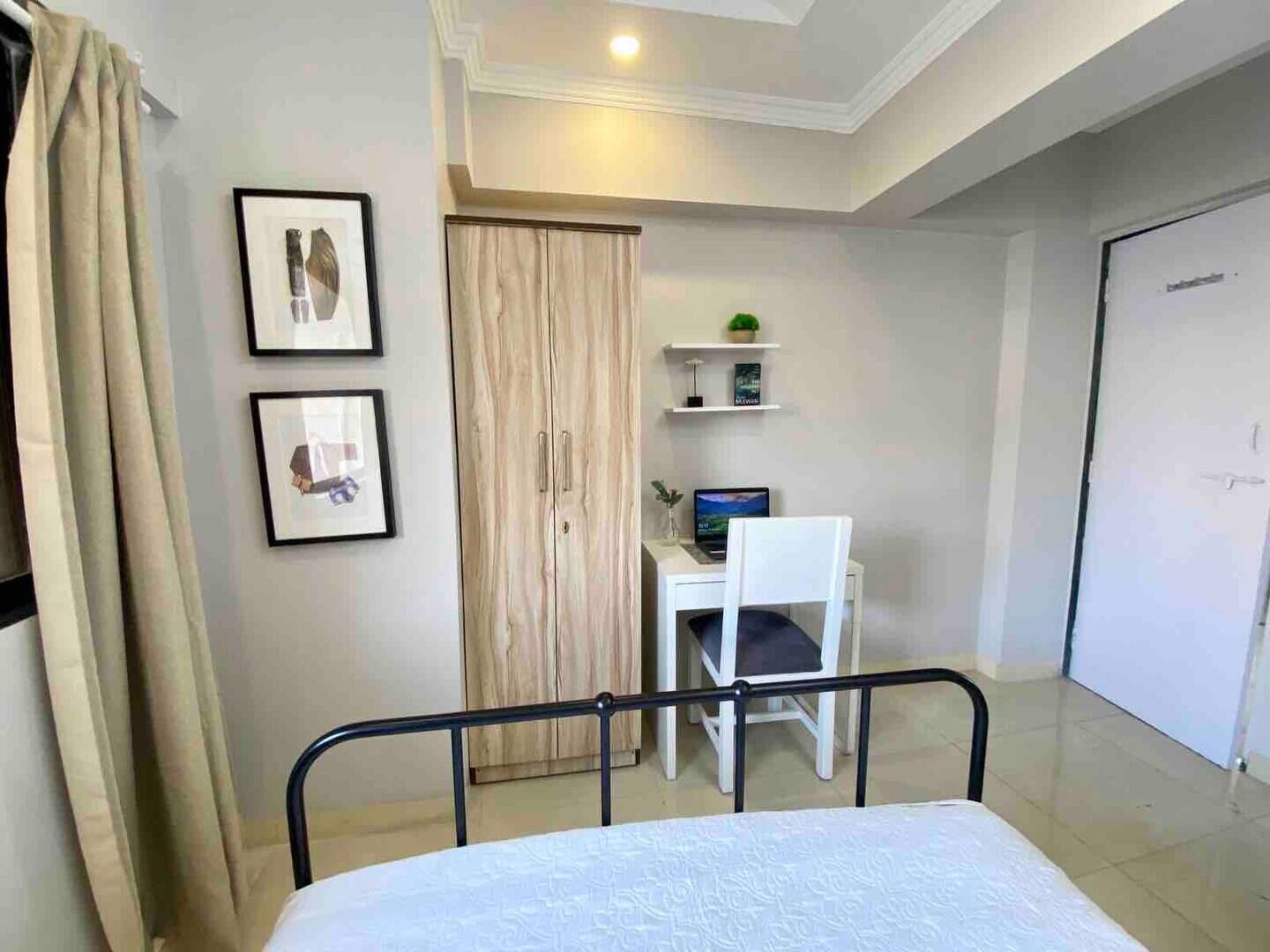 Un dormitorio con cama, escritorio y silla, armario y dos cuadros en la pared.