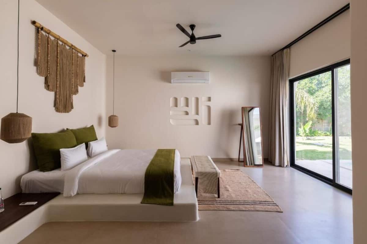 Een moderne slaapkamer met een groot bed, een plafondventilator, een airconditioning en uitzicht op de omgeving door een groot raam.