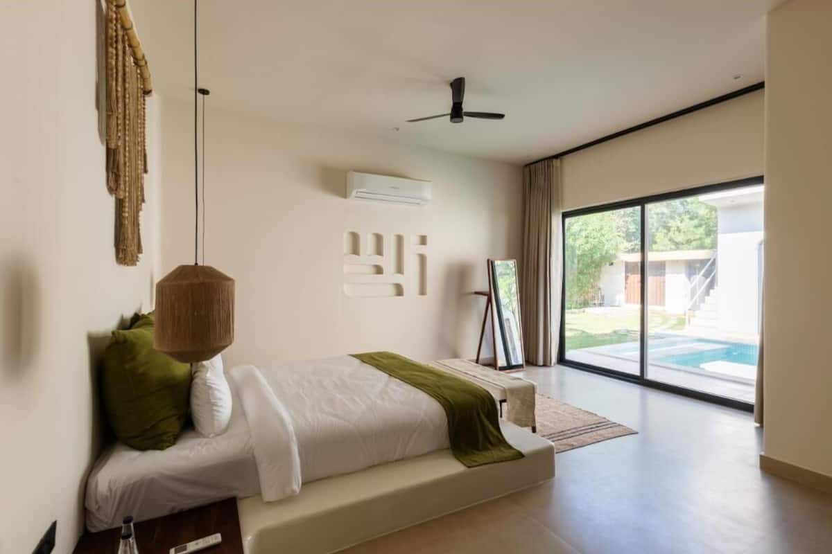 Een moderne slaapkamer met een bed, een plafondventilator, een airconditioning en uitzicht op een zwembad door grote ramen.