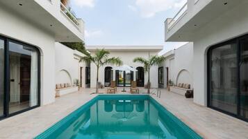 Uma área de piscina moderna com uma piscina retangular, rodeada por paredes brancas e janelas amplas.