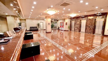 A hotel lobby with a reception desk, seating area, elevators, and a vending machine.