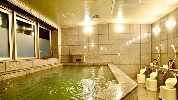 Ein Wellnessbereich mit einer großzügigen Badewanne, einer kleinen Sitzecke und einer Dusche mit mehreren Wasserhähnen.