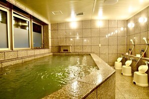 Ein Wellnessbereich mit einer großzügigen Badewanne, einer kleinen Sitzecke und einer Dusche mit mehreren Wasserhähnen.