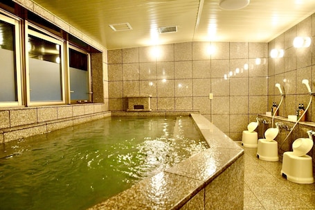 A spa area with a large soaking tub, a small seating area, and a shower with multiple faucets.